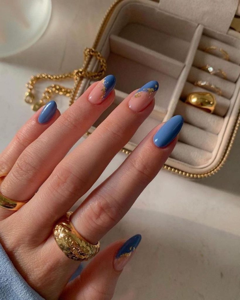 Imagen de Uñas tendencia con forma ovalada color azul, fondo color natural y detalles en dorado.