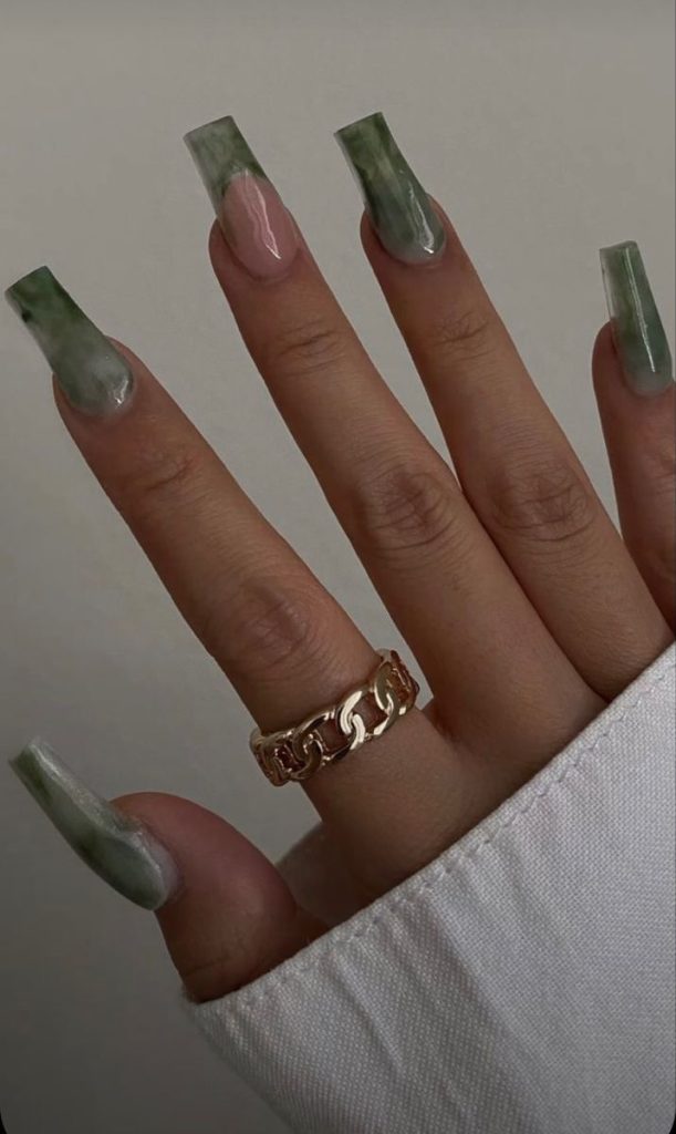 Uñas cuadradas con diseño marmolado en tonos de verde, la uña de en medio es estilo francesa.