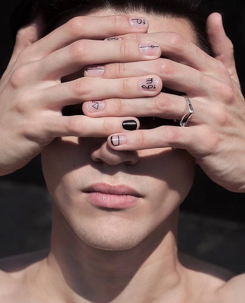 Imagen de una cara tapada por dos manos con Manicura de pequeños símbolos geométricos en negro.