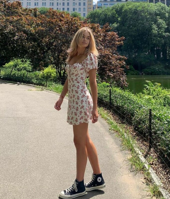 Imagen de chica en el parque parada mirando hacia un costado, tiene un vestido corto con  estampado de flores y converse negras.